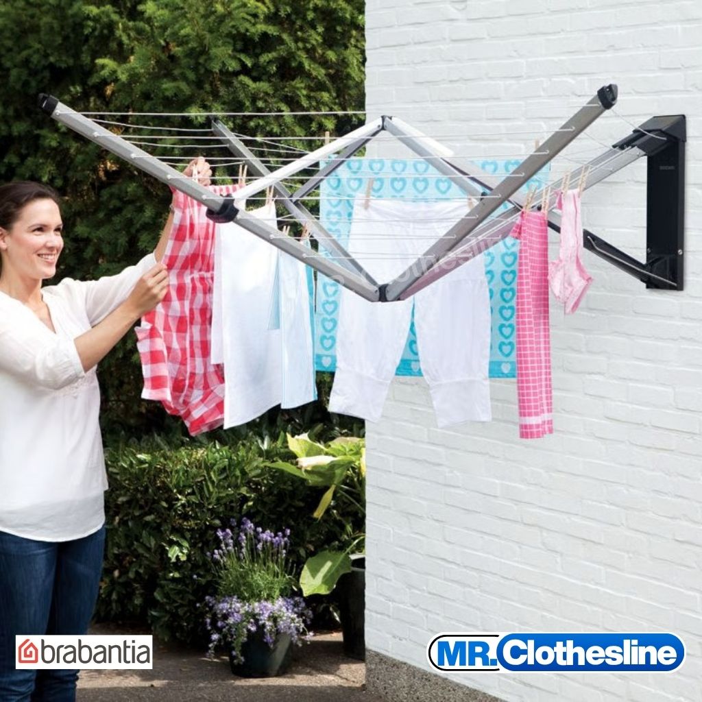 A woman hanging clothes out on the clothesline with a green backyard and the clothesline installed onto a white painted brick wall.