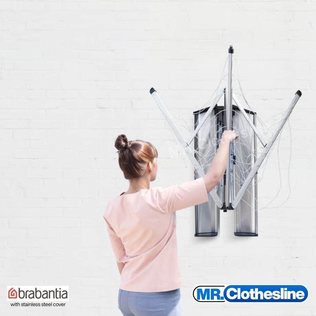 A woman mid way of opening up the wall fix clothesline with one hand.