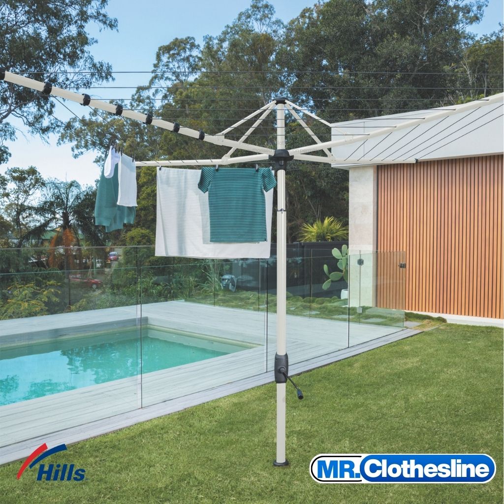 Hills Folding Rotary 7-Line Clothesline in Surfmist colour installed on lawn beside pool with washing hanging from the lines.
